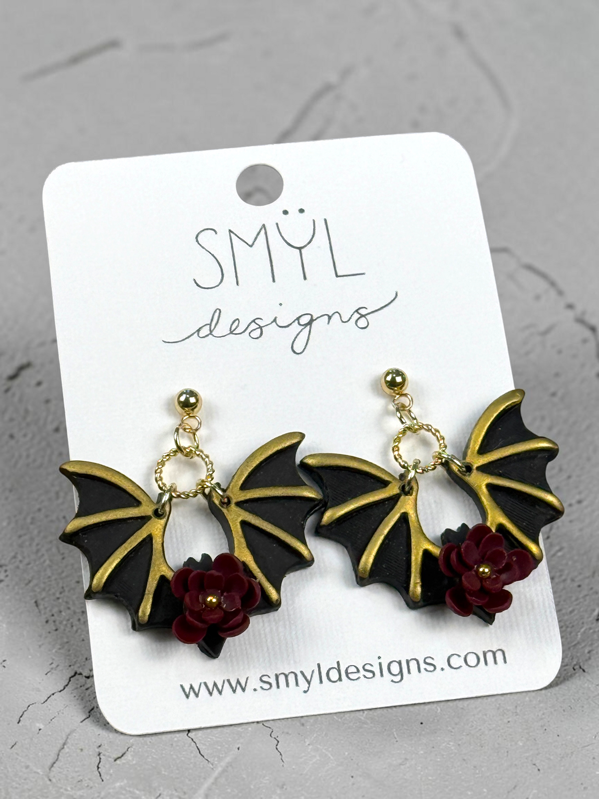 Black bat dangle earrings with gold-tone details and burgundy flowers by SMYL Designs