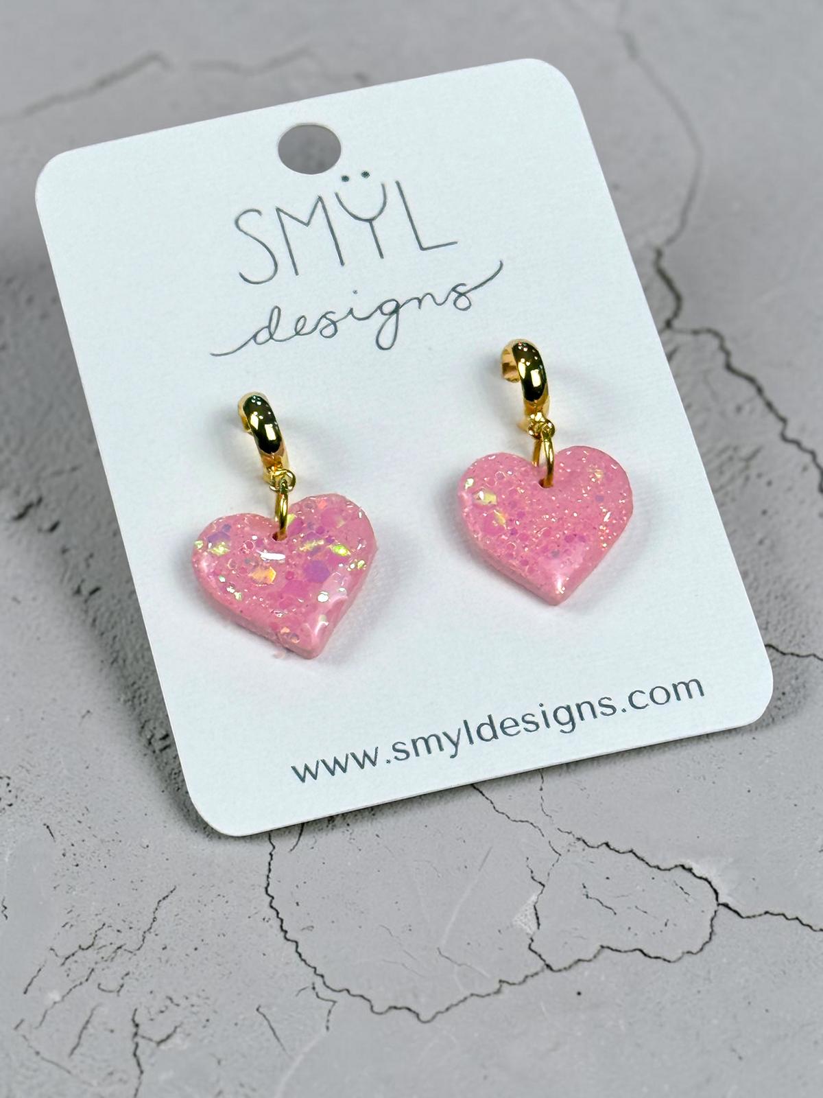 Angled view of pink glitter heart huggie dangle earrings