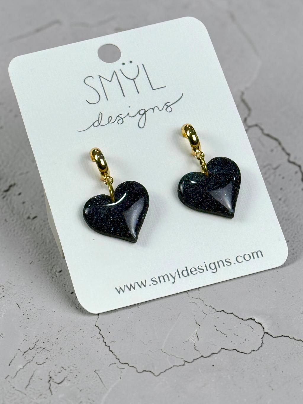 Angled view of black glitter heart huggie dangle earrings