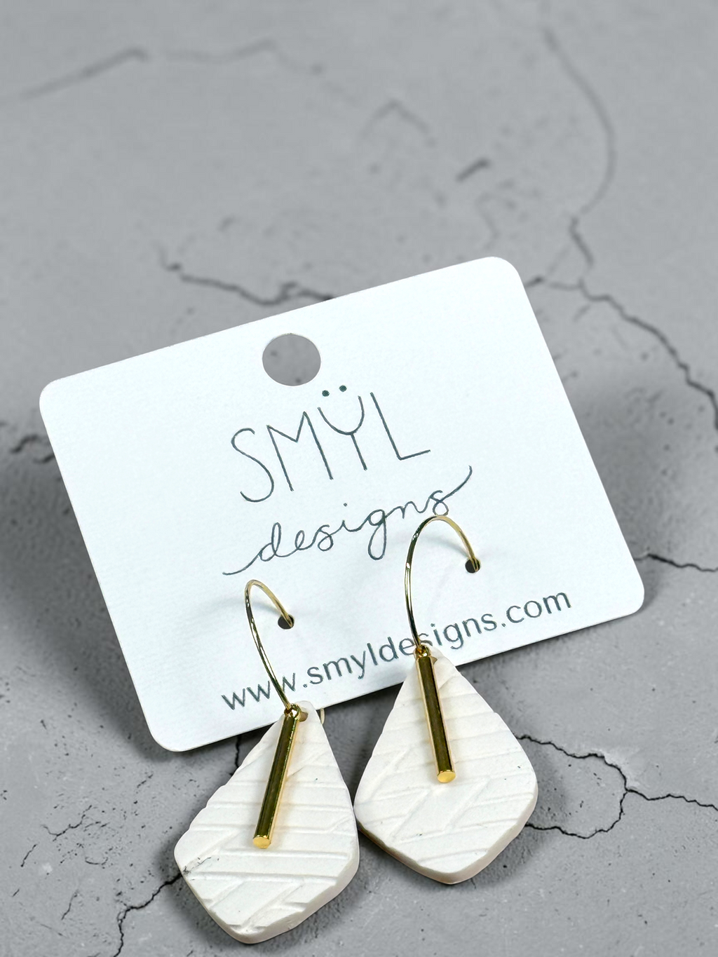 Angled view of white textured teardrop hoop dangles