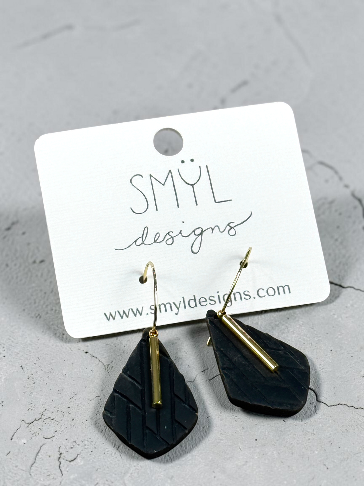 Angled view of black textured teardrop hoop dangles